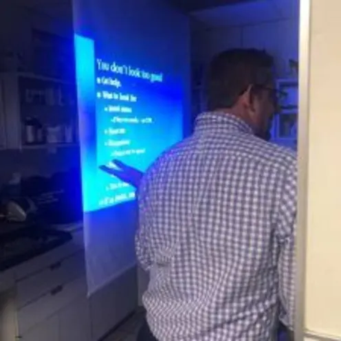 A man standing in a doorway, while someone is presenting Powerpoint slides being projected
